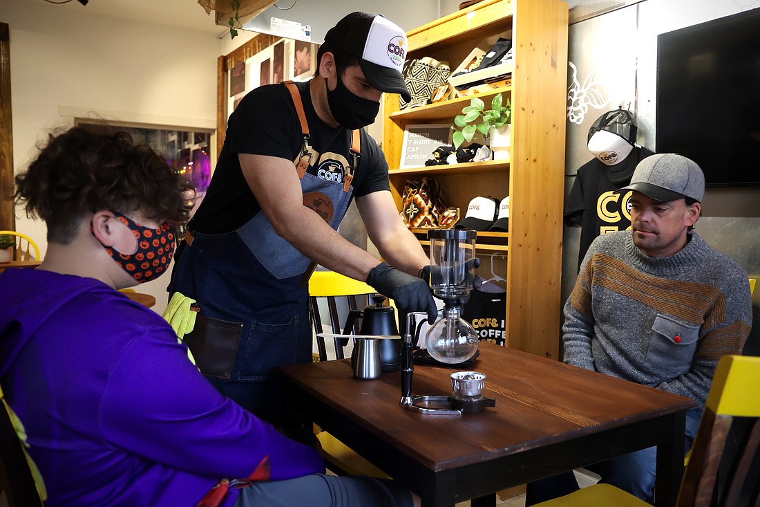 Oscar Quintero prepares a Japanese siphon brewing method for customers Ben, left, and Jon Hansen at Cof& on Feb. 22.