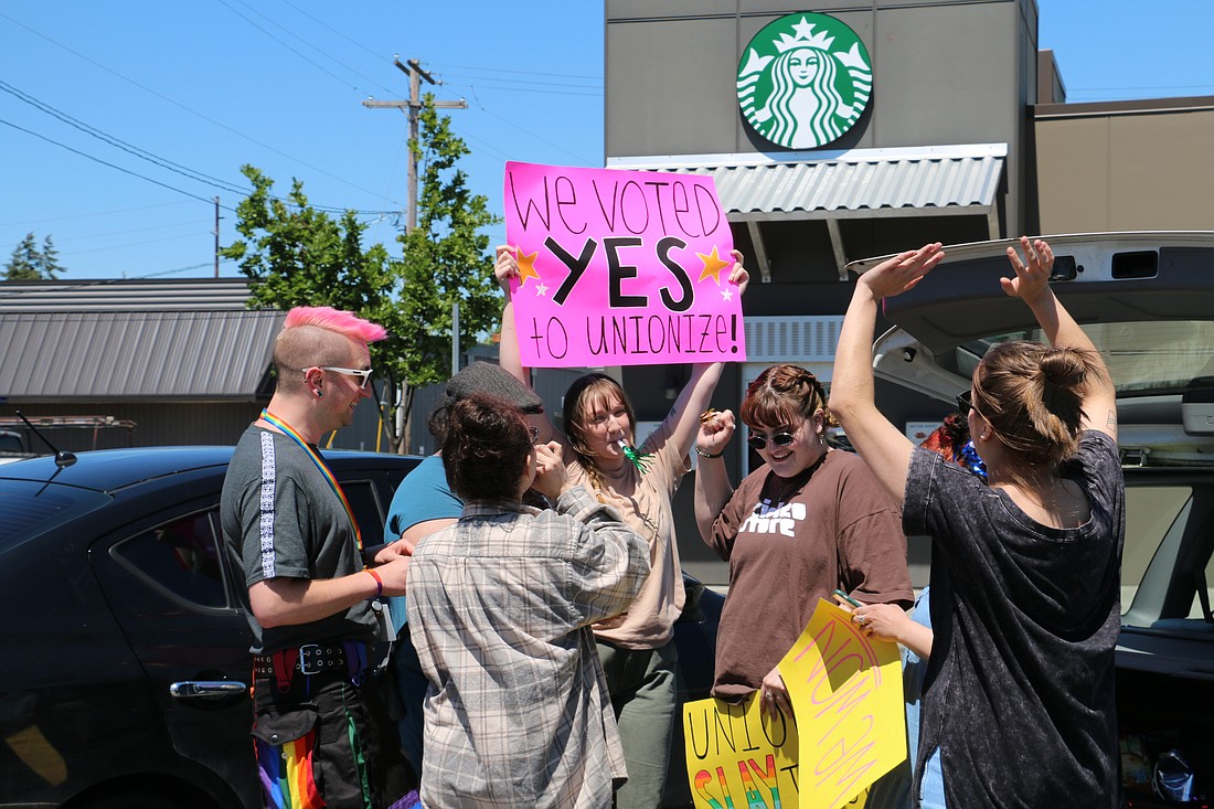 Starbucks employee Shannon Butler, center, holds up a sign as she and her coworkers celebrate a unanimous vote to unionize at the Iowa and King Street location on June 24. With each incoming "yes" vote, the off-the-clock employees tooted noisemakers.