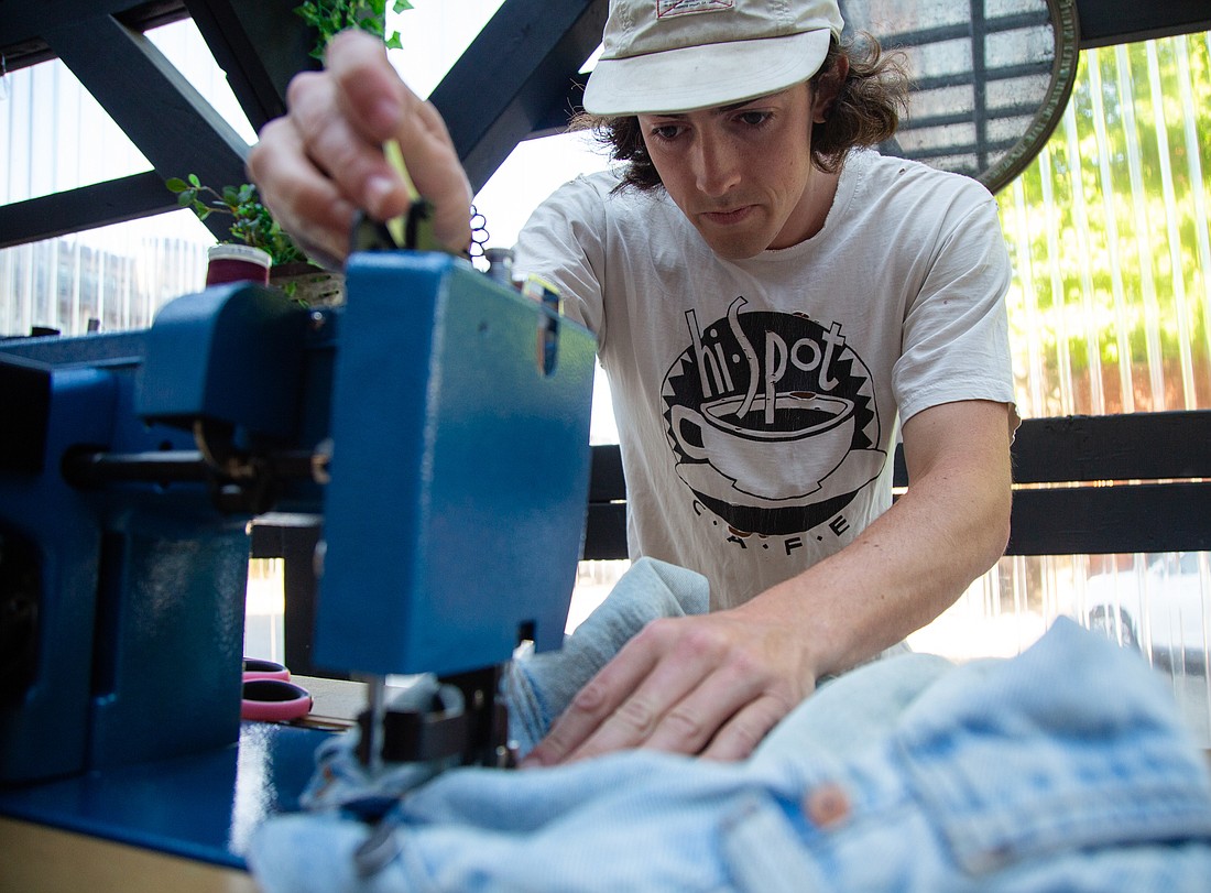 Jack Kingsley patches a hole in jeans at his mobile sewing table in the parklet at Cafe Blue on July 28. Kingsley's Guerrilla Garmentry is the result of his senior project at Fairhaven College and his volunteer mending at Ragfinery.