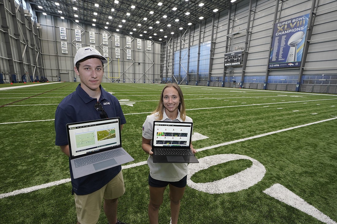 Peter Engler, left, a football research assistant, and Becca Erenbaum, a senior football research analyst, hold laptop computers as they pose for a photo on Aug. 3 at the Seattle Seahawks' NFL football indoor training facility in Renton, King County.