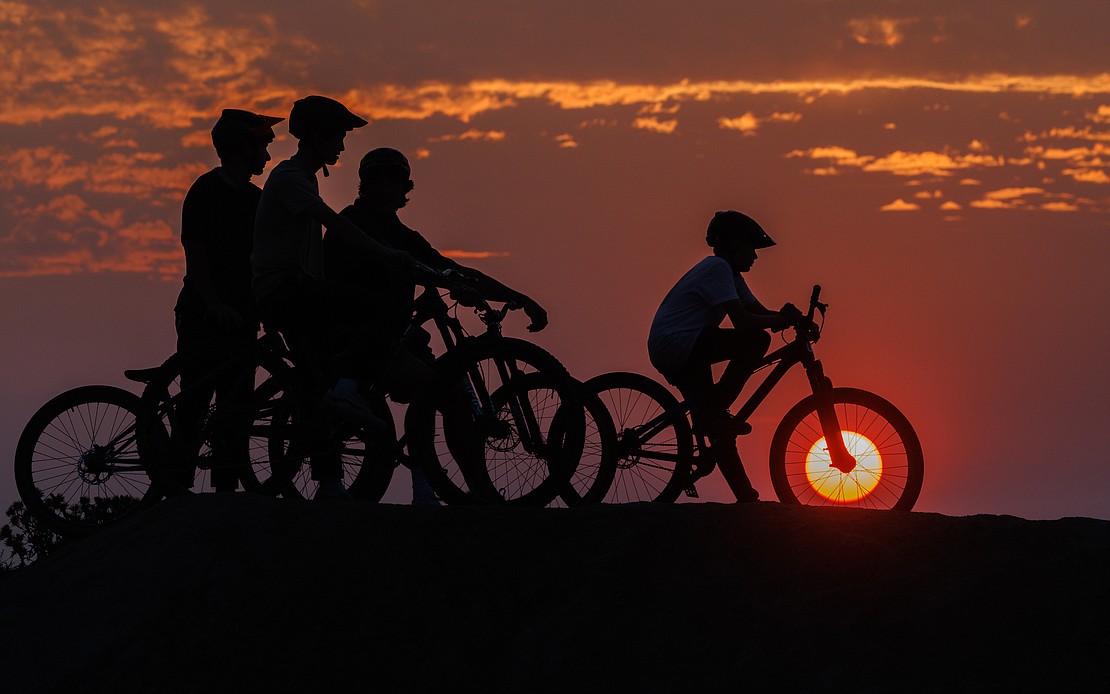 A red sun sets inside a bike rim as pump track riders wait their turn to ride on Sept. 11. Smoke from regional wildfires is expected to hang around this week.