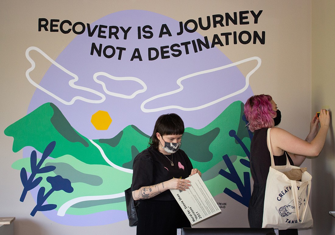 Jessyca Murphy, left, and Emily Campbell hang a plaque crediting Stevie Shao for one of the murals painted at the Whatcom County Crisis Center on July 15.