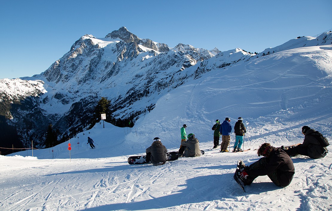 Snowboarders strap on their boards with Mount Shuksan towering above.