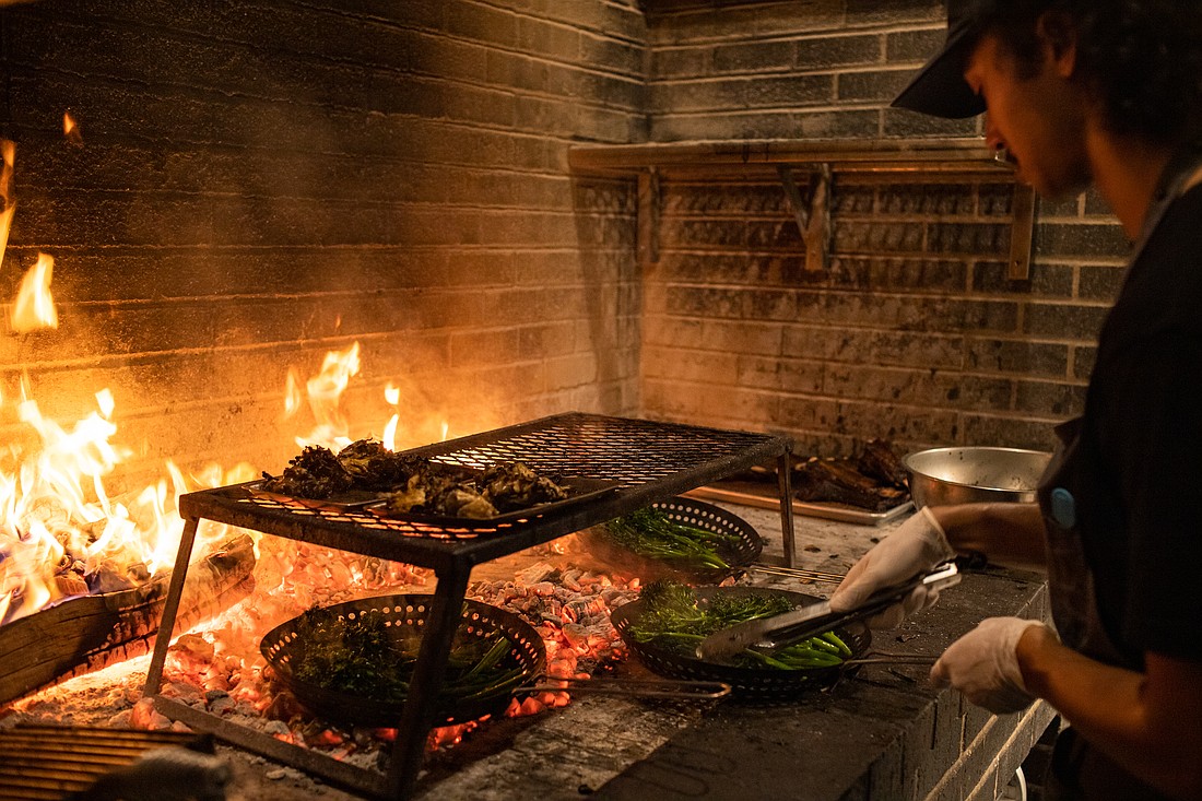 Jared Jones roasts broccolini and meat over coals on a wood fire at Carnal on Nov. 19. The restaurant relies on live fire to cook many of its dishes.