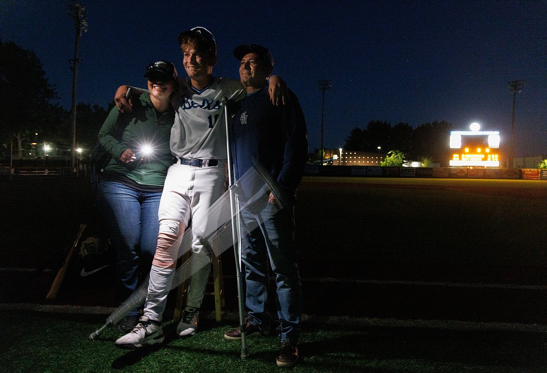 As one of his crutches falls to the ground, Bellingham Bells player Blake Conrad gets a photo taken with parents Tiffani Mauro and Tim Conrad, right, after the field lights were turned off during a post-game autograph session with fans on Aug. 4. Blake injured his knee during the 8-3 win over the Victoria HarbourCats.