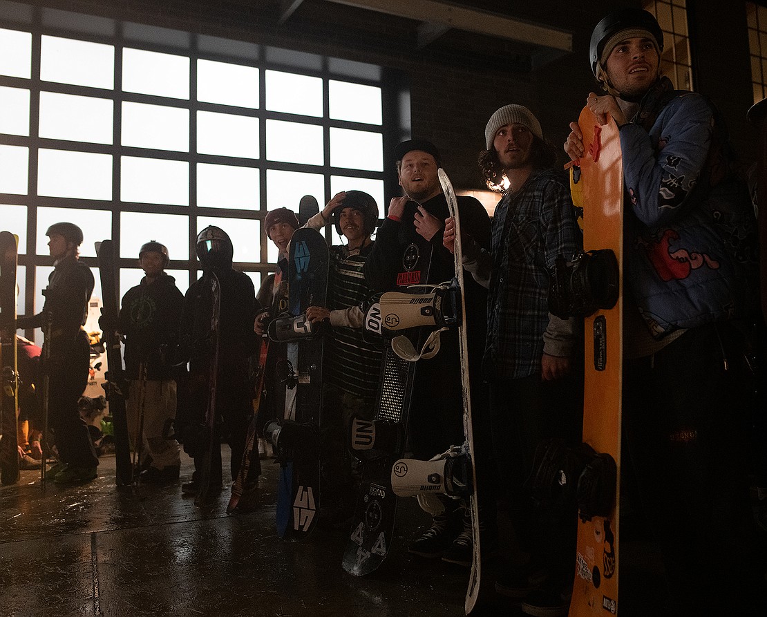Snowboarders and skiers wait in line for their turn.