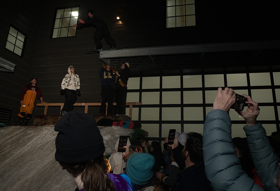 The crowd films as a snowboarder leaps from a steel beam above the ramp.
