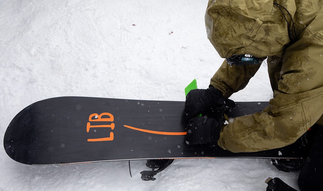 A snowboarder waxes their board before their race.