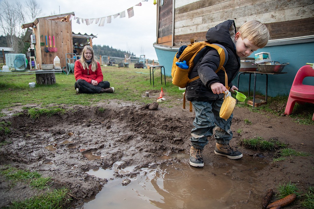 Teacher Lizzy Chandler, left, watches Mac play in the mud pit Feb. 13 at Barefeet Farm School. The outdoor school, which just became licensed thanks to a 2021 state law, operates year-round, rain or shine.