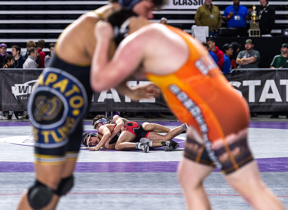 A 1A match is pictured in the background as Blaine’s Victor Gervol, in the orange singlet, competes against Wapato’s Angel Leyva.