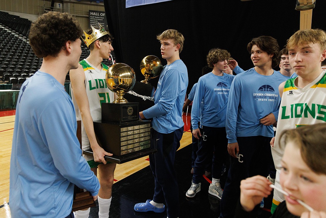 Lynden’s Anthony Canales, wearing a crown, and Lynden Christian’s Jeremiah Wright talk while holding championship trophies.