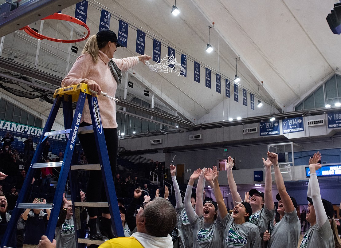 Western women's basketball coach Carmen Dolfo holds up a piece of the net as her players cheer.