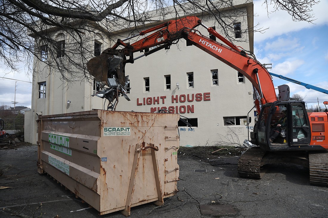 An excavator drops scrap metal into a bin March 14 at the start of demolition of the old Lighthouse Mission Ministries building.