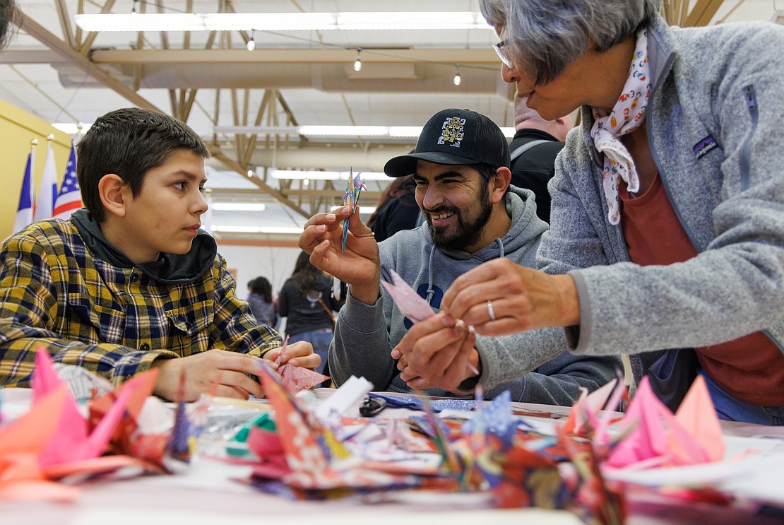 Antonio Gallegos is all smiles as he shows off his almost-finished crane during an origami lesson at the Ferndale Japanese Cherry Blossom Festival in the Pioneer Pavilion Community Center on March 18 in Ferndale. His son Aron, left, looks on as Cheryl Seminara instructs others how to make the cranes.