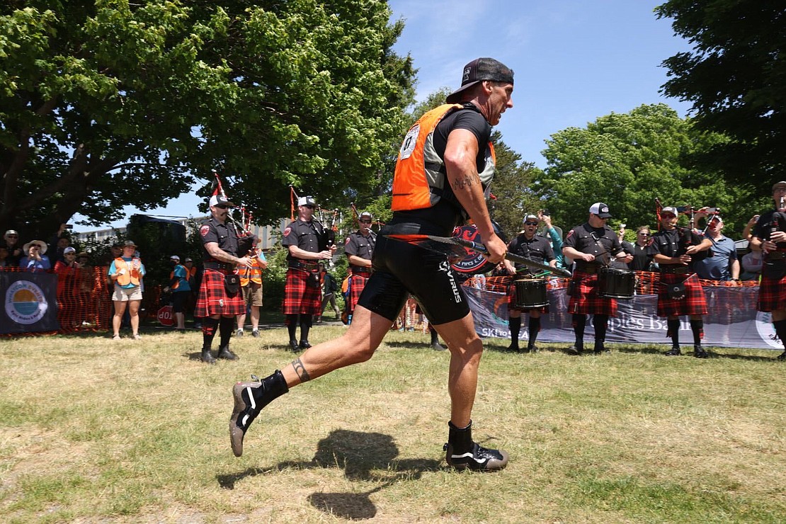 Beau Whitehead of Bellingham Firefighters Whatcom Open Team runs to the finish line as the Bellingham Firefighters Pipes and Drums play behind him.