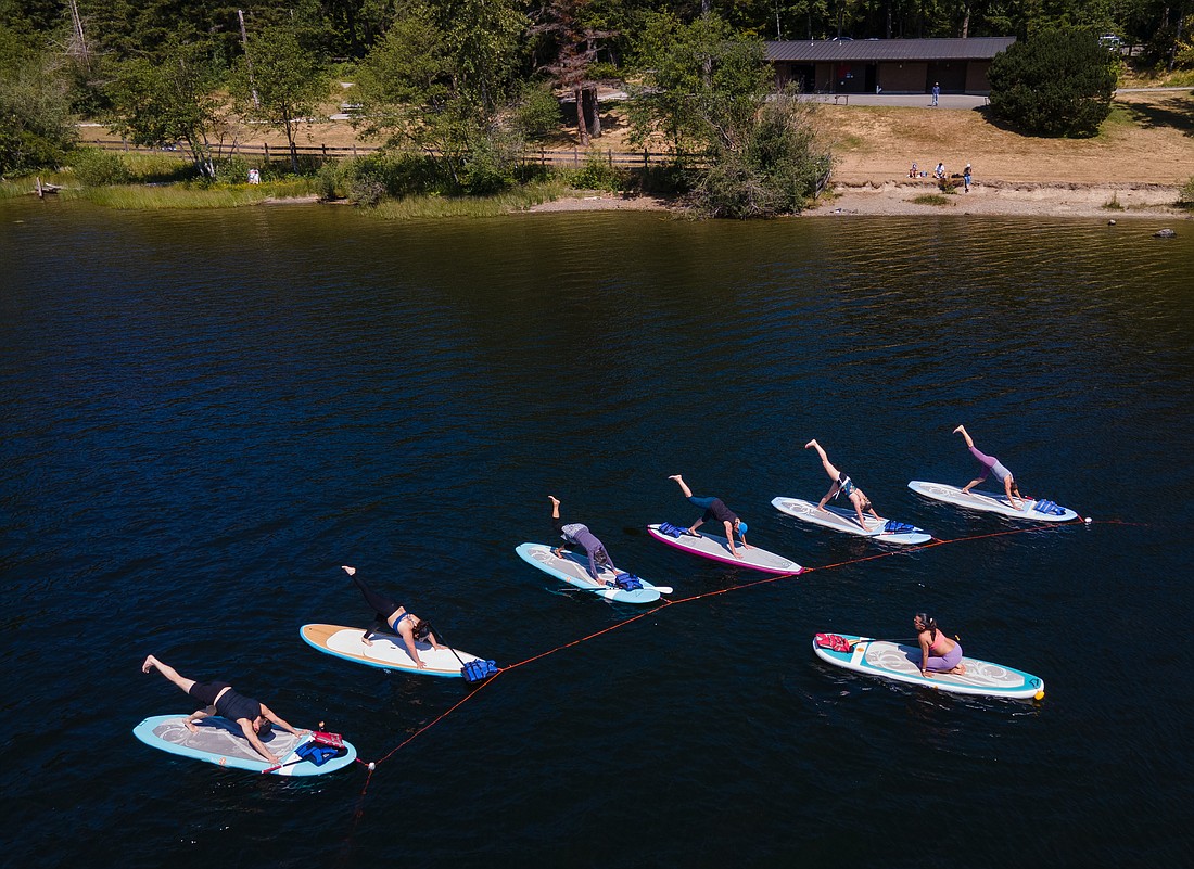 Paddleboarders bend into the one-legged downward-facing dog pose during stand-up paddle yoga July 11 at Lake Padden. Instructor Melissa Longfellow from Flux Power Yoga anchors a line and connects the paddle boards to the line to keep the group together.