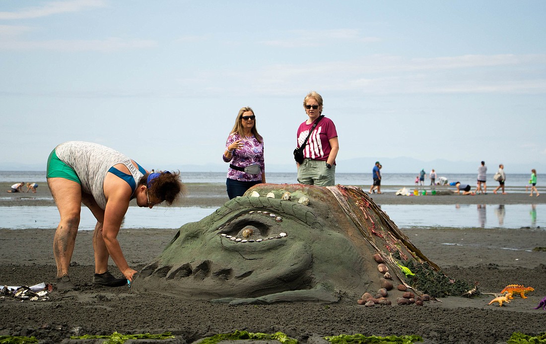 Onlookers at the Birch Bay Sand Sculpture Competition admire the prehistoric-themed sculpture July 29, decorated with plastic dinosaurs and seashell scales, and designed by Leo Vulama.