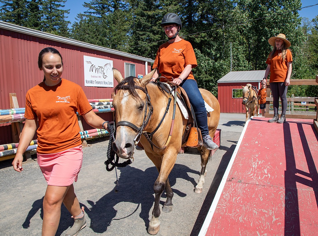 Volunteer Nota Tsitsiragos, left, leads Michelle Tremblay on Leonardo from the ramp mounting station as program director Hilary Groh watches Aug. 15 at the Northwest Therapeutic Riding Center. The center provides recreational riding classes for dozens of people with disabilities each year.