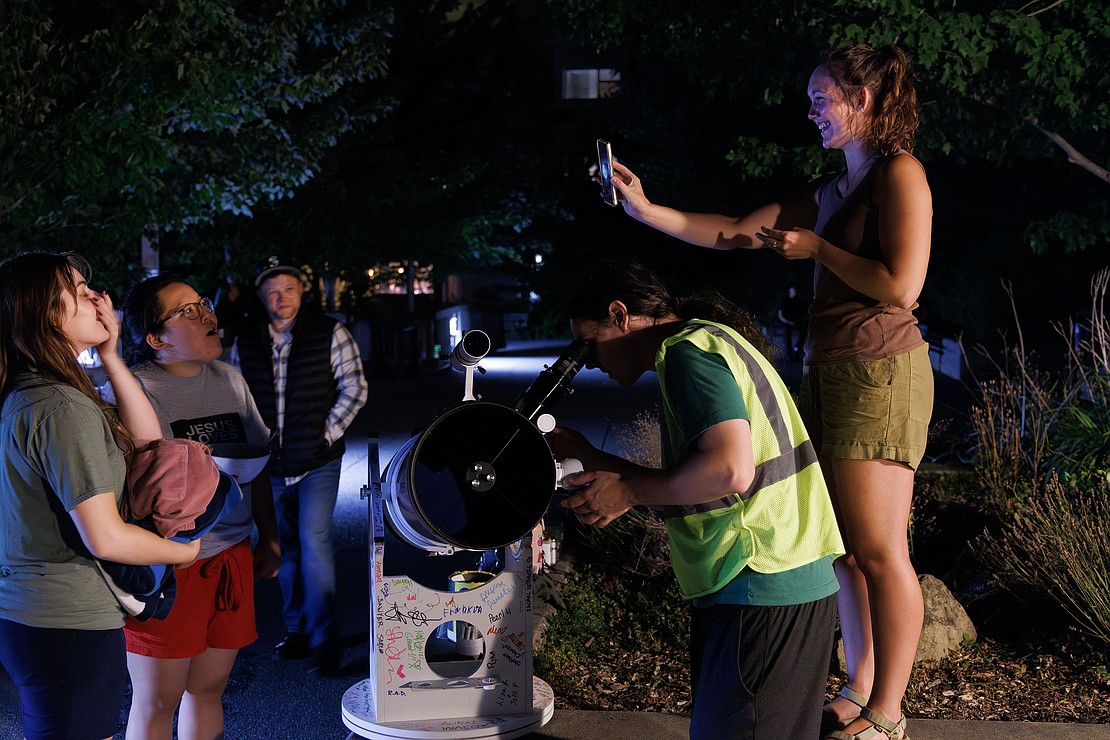 Friends react as Tessa Brusven, right, shows off a cellphone photo of the moon while Robert Wilmore adjusts his 10-inch Newtonian telescope Sunday, Aug. 27 at Taylor Dock in Bellingham. The cellphone photo was taken by Wilmore through the eyepiece of his telescope.