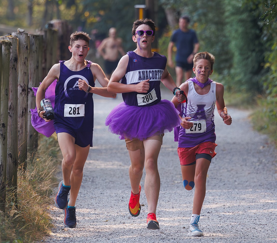 Maverick Ball, left, and Owen Kennedy, right, run with teammate Owen Hofheimer Aug. 26 as he runs the final lap for the team at the Lake Padden Relay in Bellingham. The race is four 2.59-mile laps around the lake, or a solo run, hosted by the Greater Bellingham Running Club.