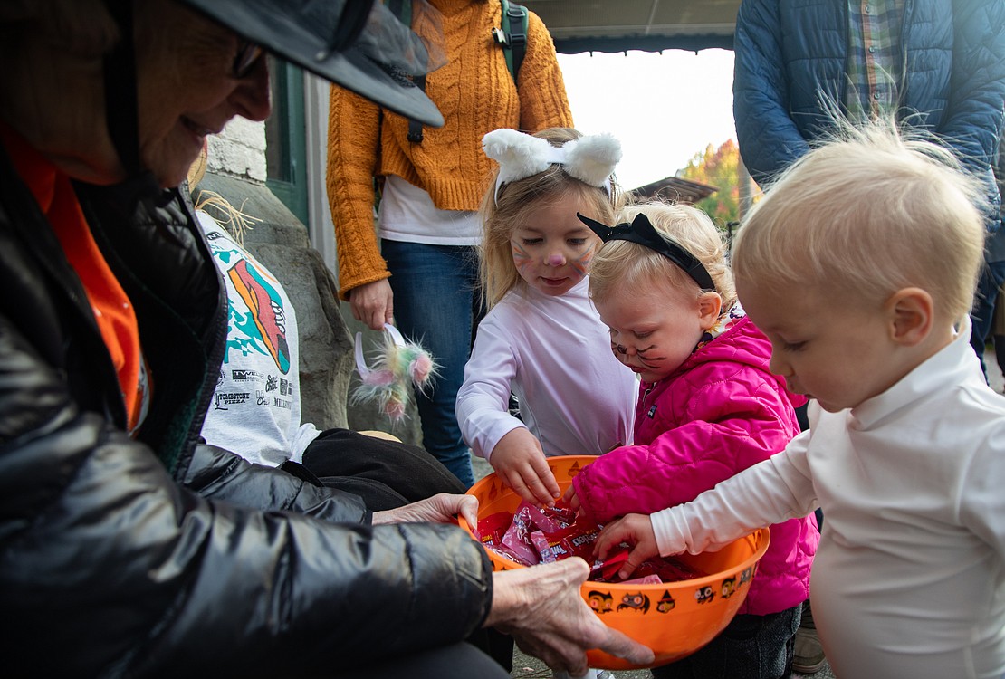 From left, Gretchen Pfueller hands out candy to Alma Loomis, 4, Linnaea Fredrickson, 2, and Owin Loomis, 2, outside of Fairhaven Runners and Walkers.