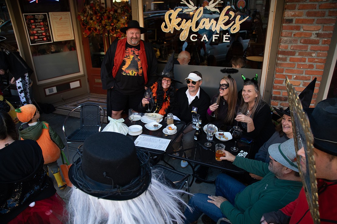 A group of friends watches trick-or-treaters pass by while dining out in front of Skylark's Cafe.
