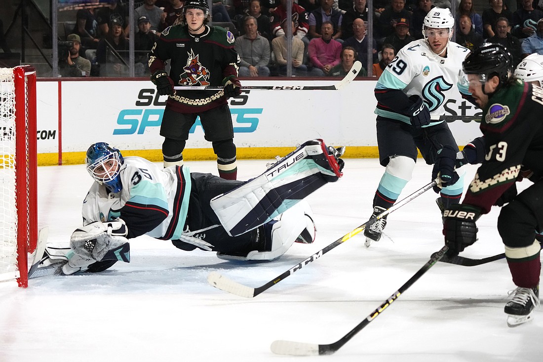 Seattle Kraken goaltender Joey Daccord, left, makes a diving save on a shot by Arizona Coyotes left wing Michael Carcone, right, as Kraken defenseman Vince Dunn (29) and Coyotes center Logan Cooley, back left, look on during the first period of an NHL hockey game Tuesday, Nov. 7, 2023, in Tempe, Ariz.