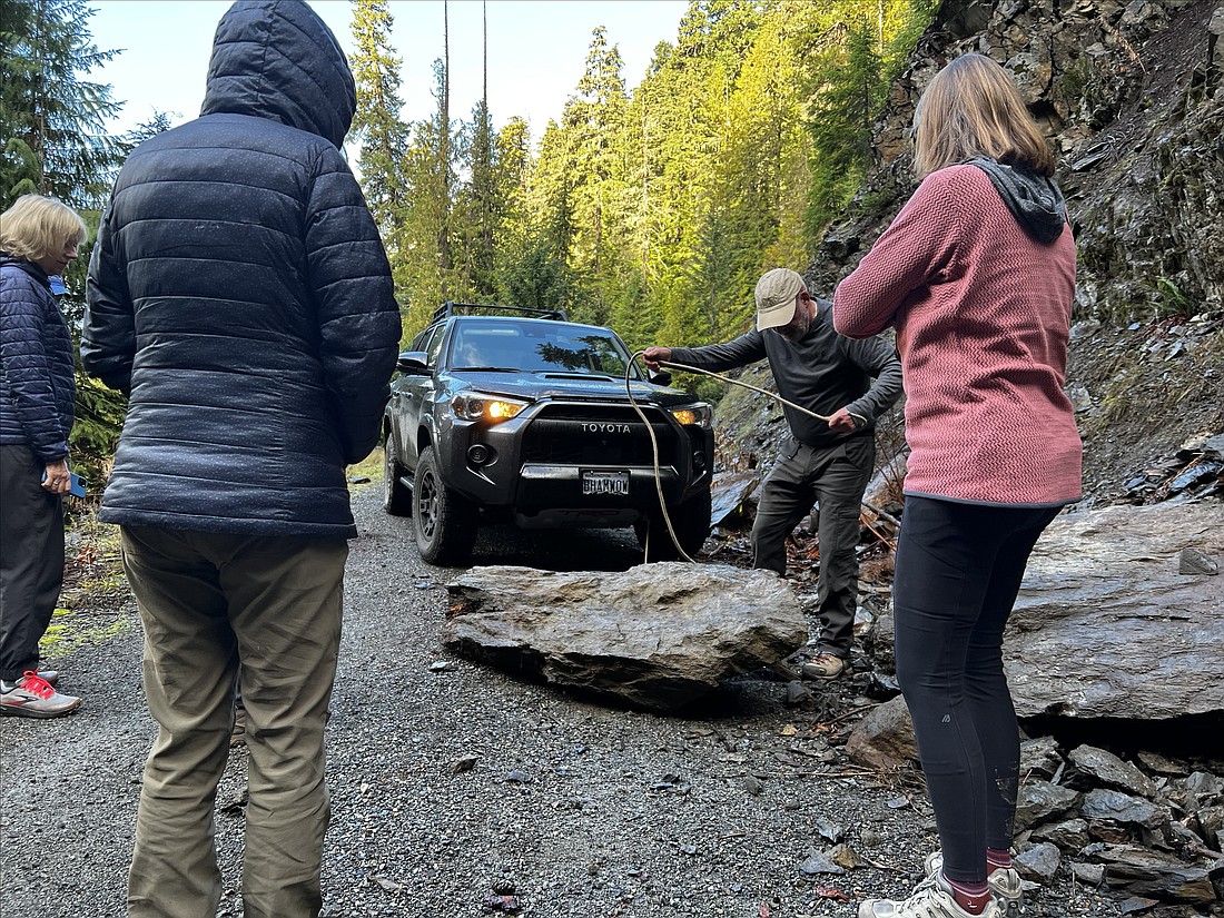 The group watches Vernon Brown of Bellingham fasten a rope to a fallen rock blocking a forest service road in the Central Cascades.
